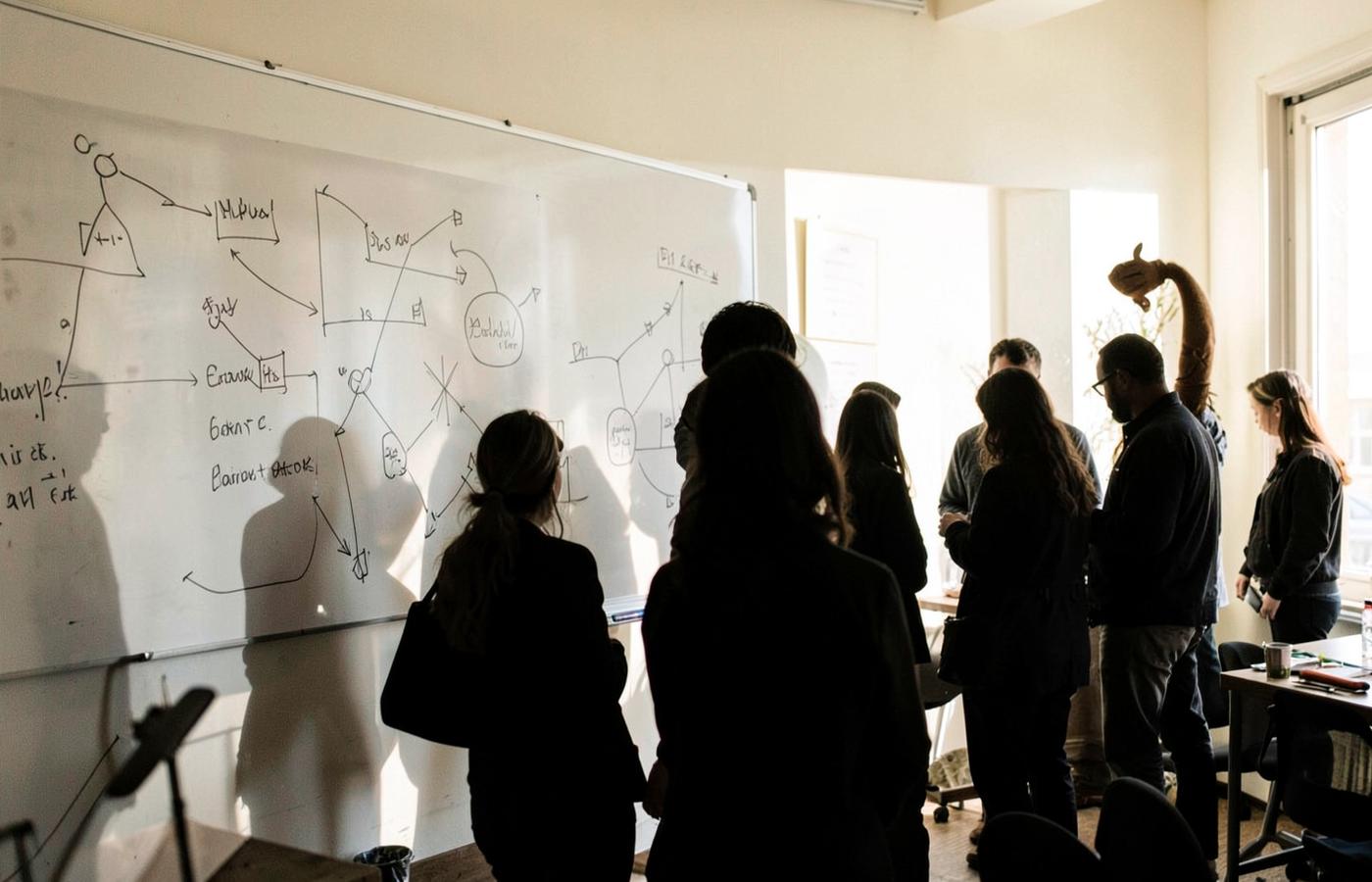 People discussing diagrams at a whiteboard, an illustrative collaborative working session